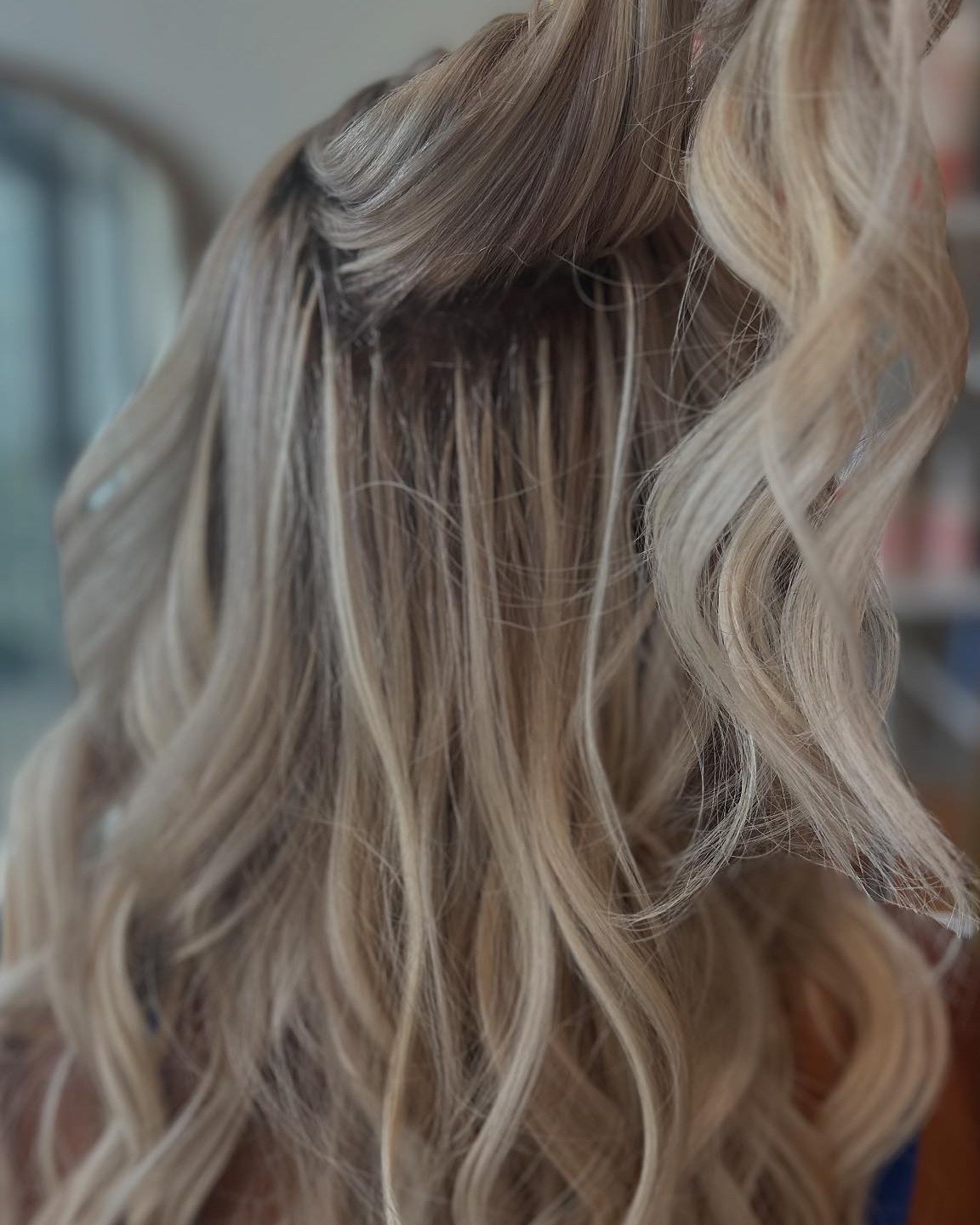 A close view of blonde waves where 22-inch K-tip extensions by Tori Knox blend into the client's own hair at the root, at Canterbury & Co. in Fort Myers.