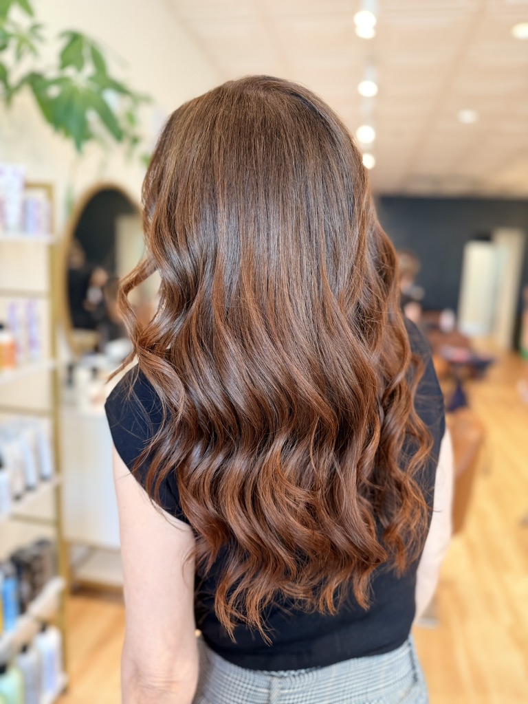 Rich dimensional brunette with warm copper tones through long curled waves, seen from behind, from the Canterbury & Co. portfolio.