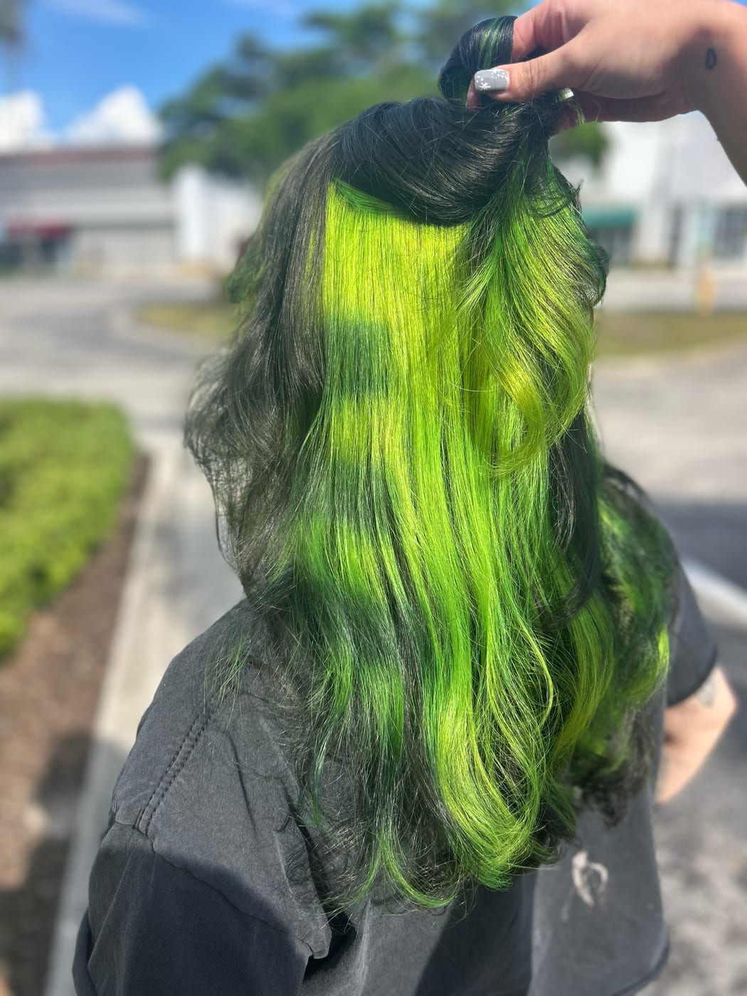 Top section of long black hair lifted to reveal a lime-green peekaboo underlayer. Vivid color by Tori Knox at Canterbury & Co. Salon in Fort Myers