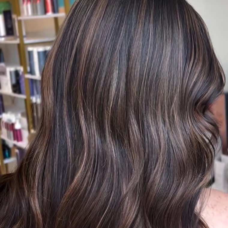 Fine ribbons of dimensional balayage through dark brunette waves, showing seamless blending from behind