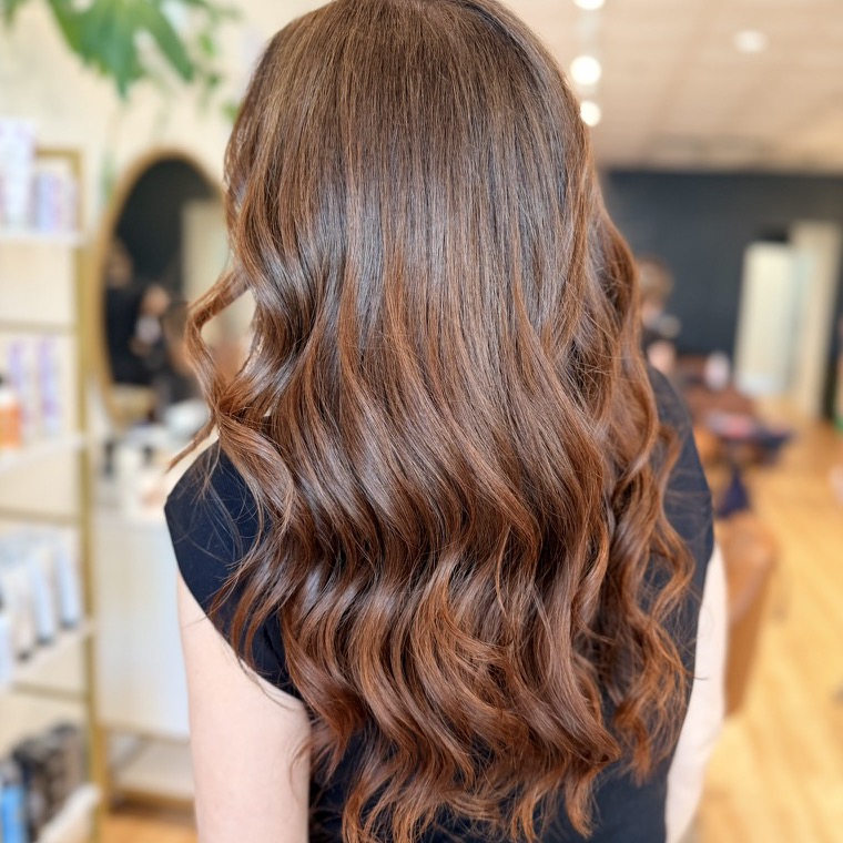 Rich dimensional brunette color with warm copper tones in long curled waves, seen from behind