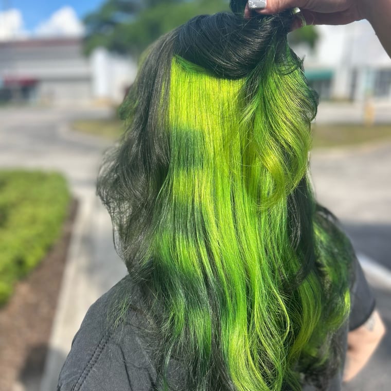Top section of long black hair lifted to reveal a lime-green peekaboo underlayer. Vivid color by Tori Knox at Canterbury & Co. Salon in Fort Myers