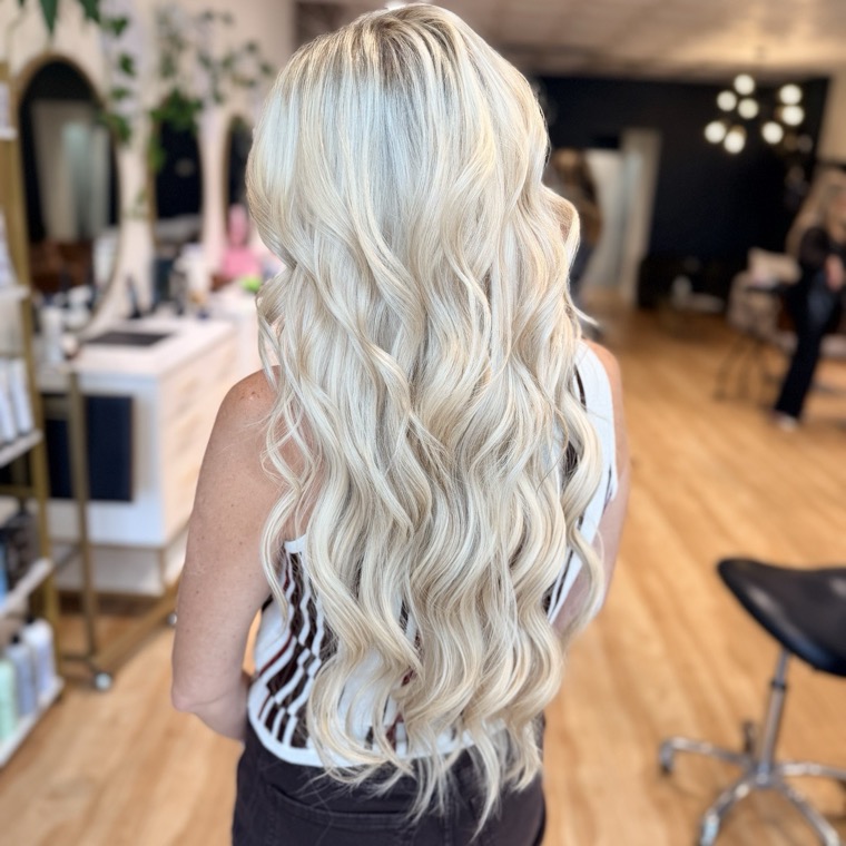 Long, full blonde hair extensions styled in soft waves, seen from behind