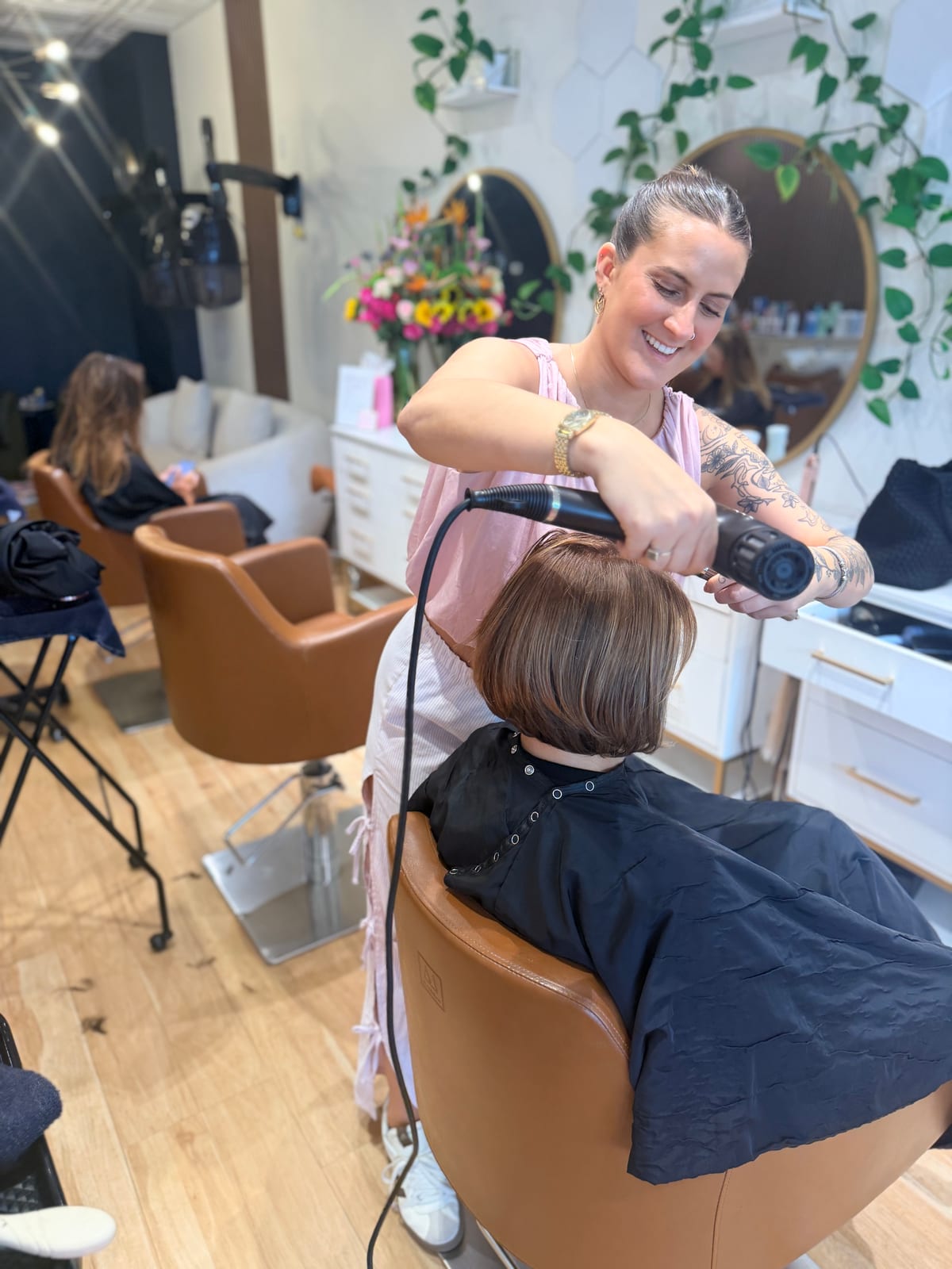 A Canterbury & Co. stylist finishing a chin-length bob with a blow-dryer and round brush.