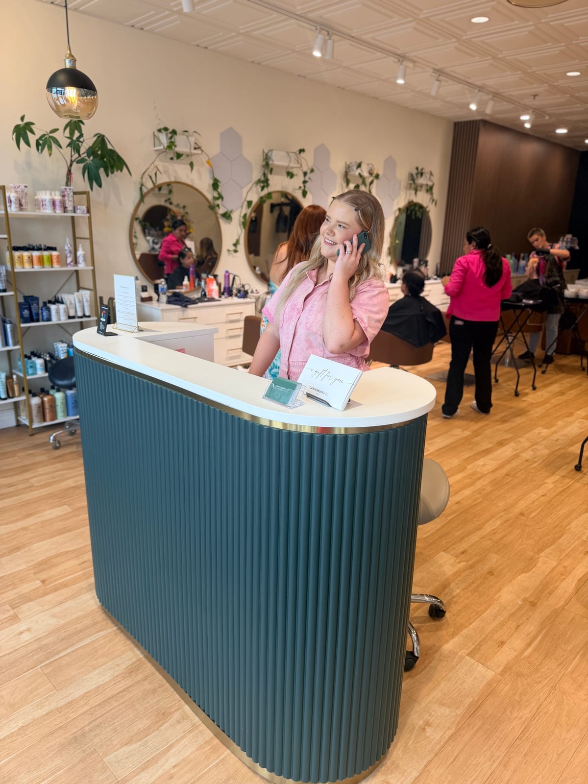 The reception desk at Canterbury & Co. with the salon floor busy behind it, stylists working at every station.