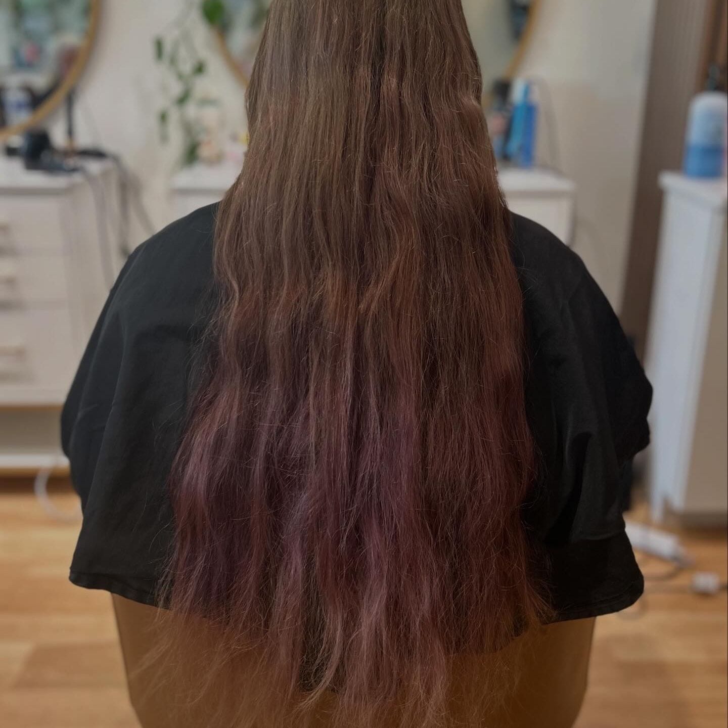 Before color correction: long hair dark with layered purple and black box dye, seen from behind in the salon chair