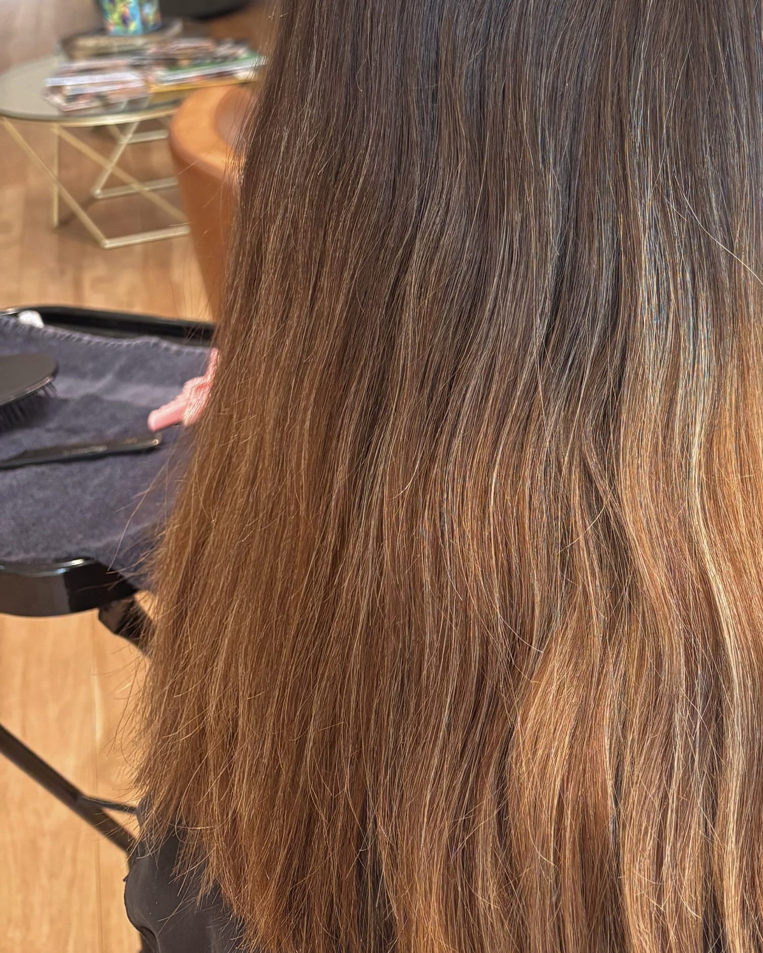 Before: long brown hair with faded orange, brassy ends, seen from behind in the salon chair