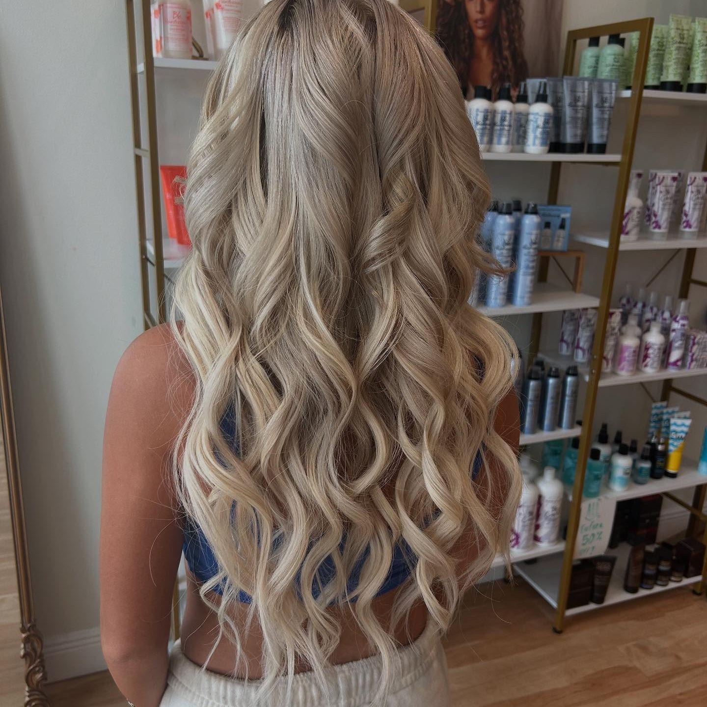 After: long blonde hair with 22-inch K-tip extensions, finished in loose waves, seen from behind in the salon