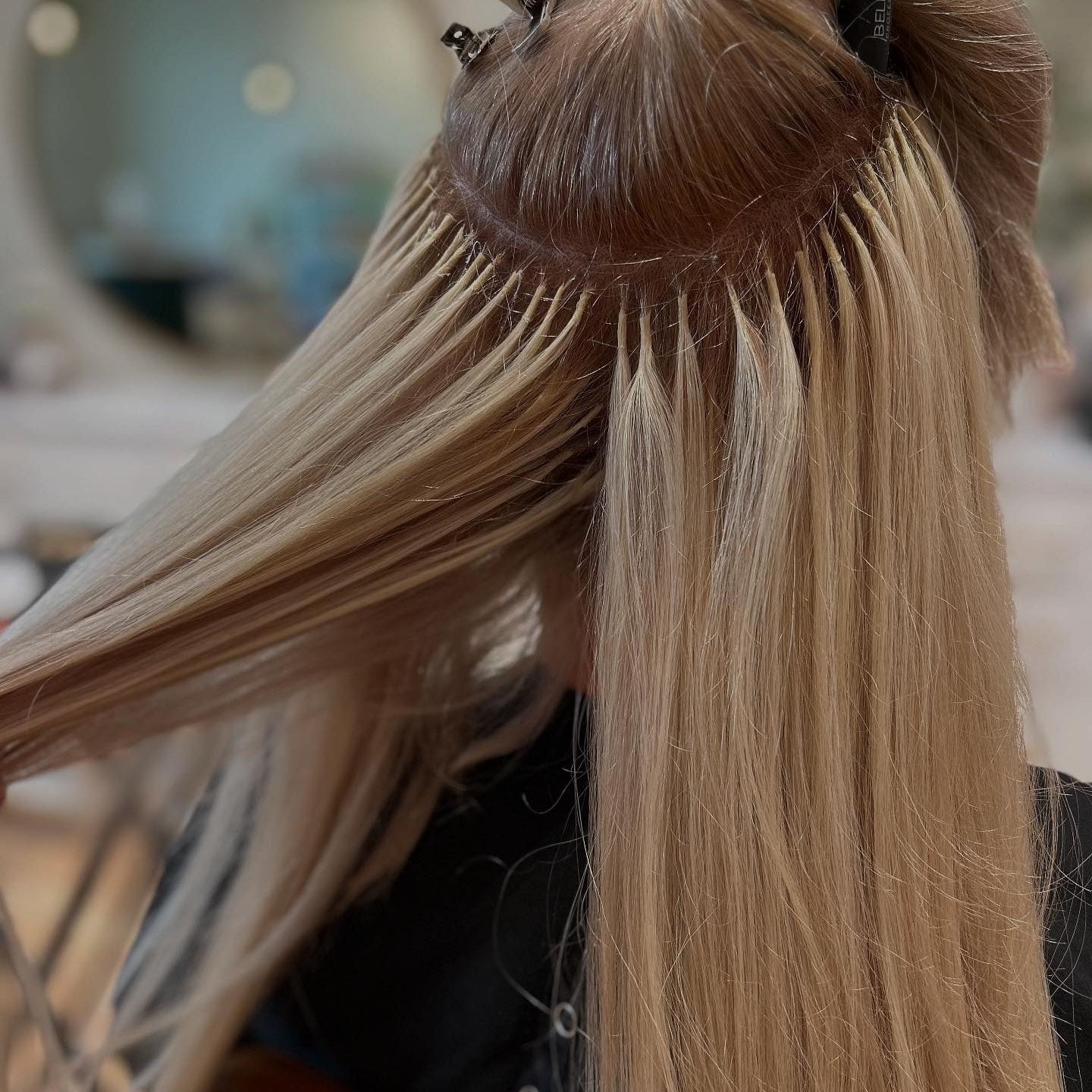 A closer view of individual K-tip bonds sitting flat near the scalp under a clipped-up section of blonde hair