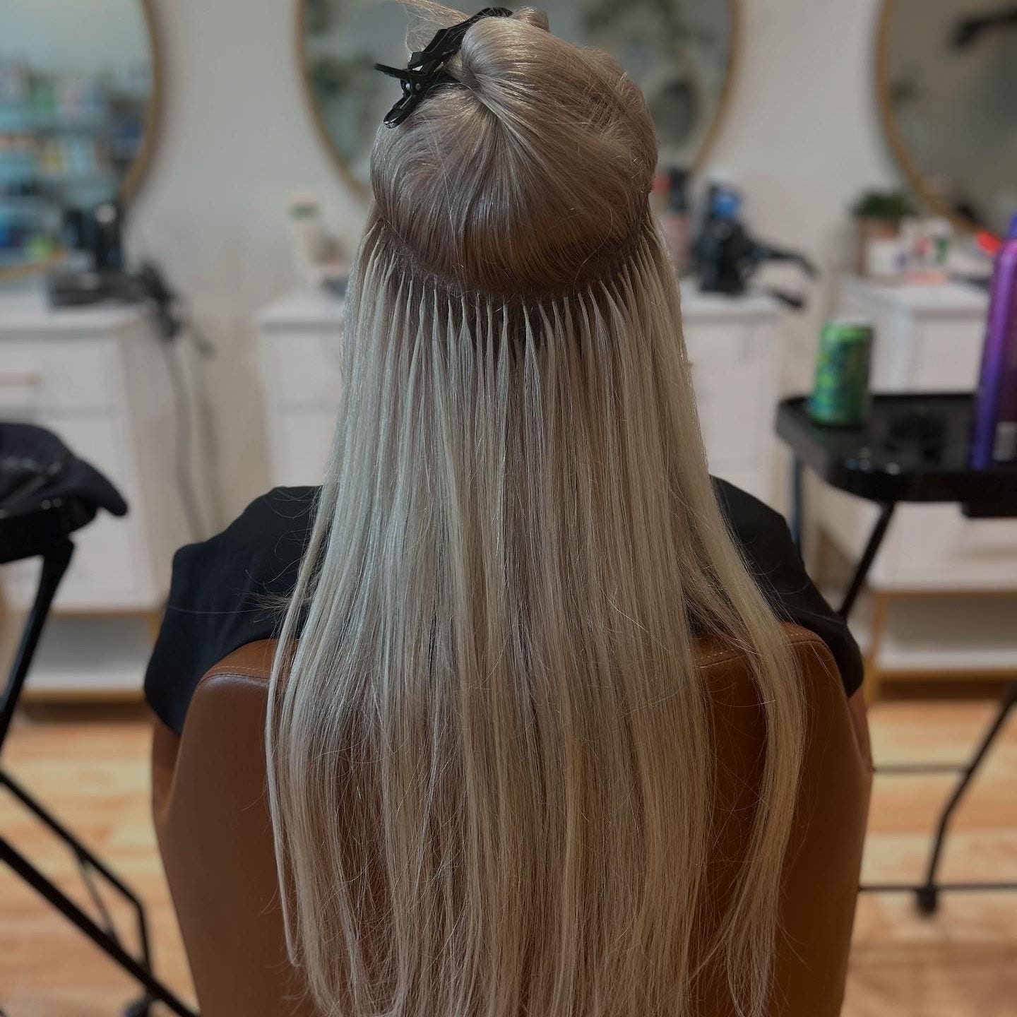 Mid-install: rows of small K-tip keratin bonds placed beneath a sectioned-up crown, with the blonde lengths falling straight