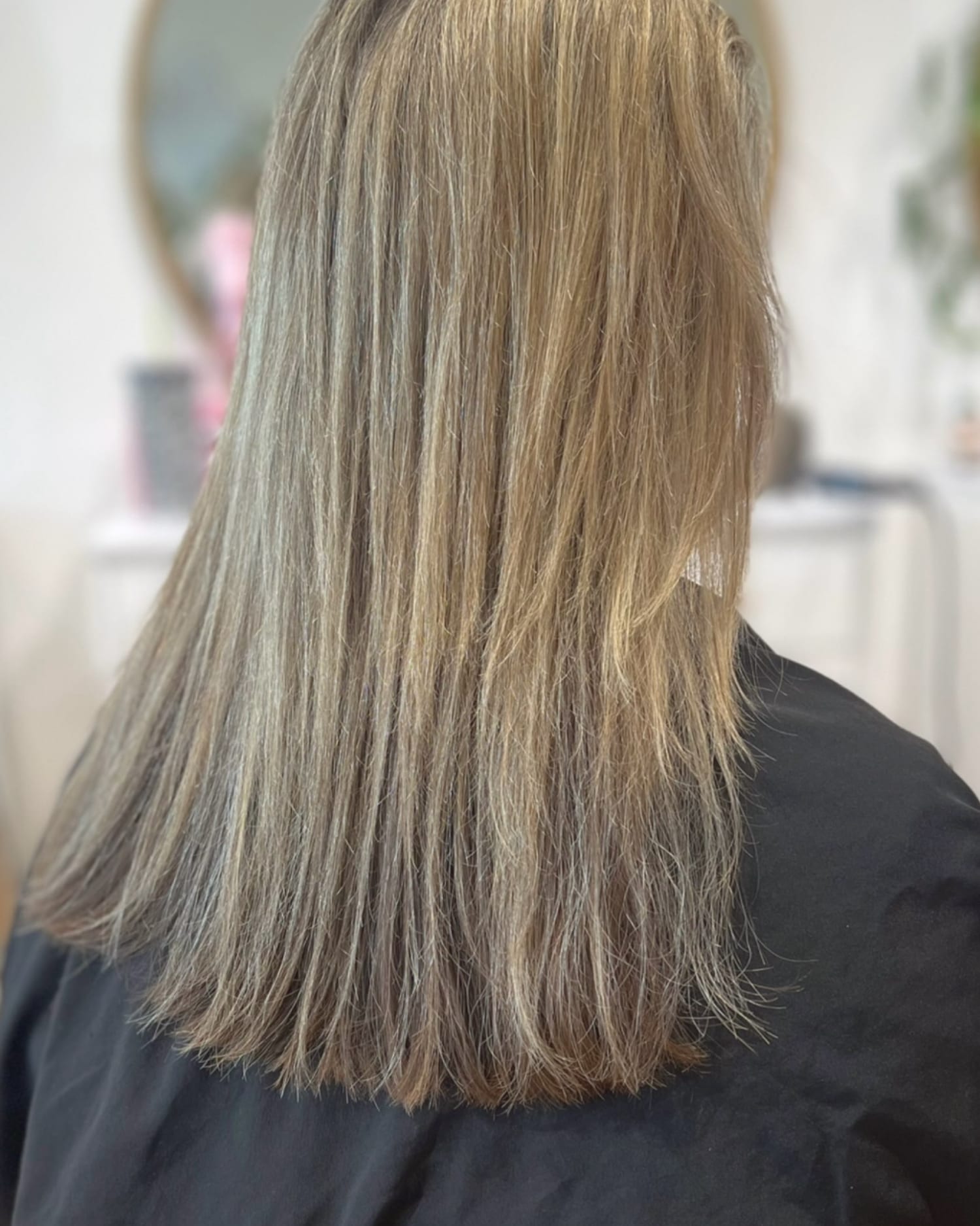Before a haircut: shoulder-length blonde hair hanging straight and flat at the ends, seen from behind in the salon chair