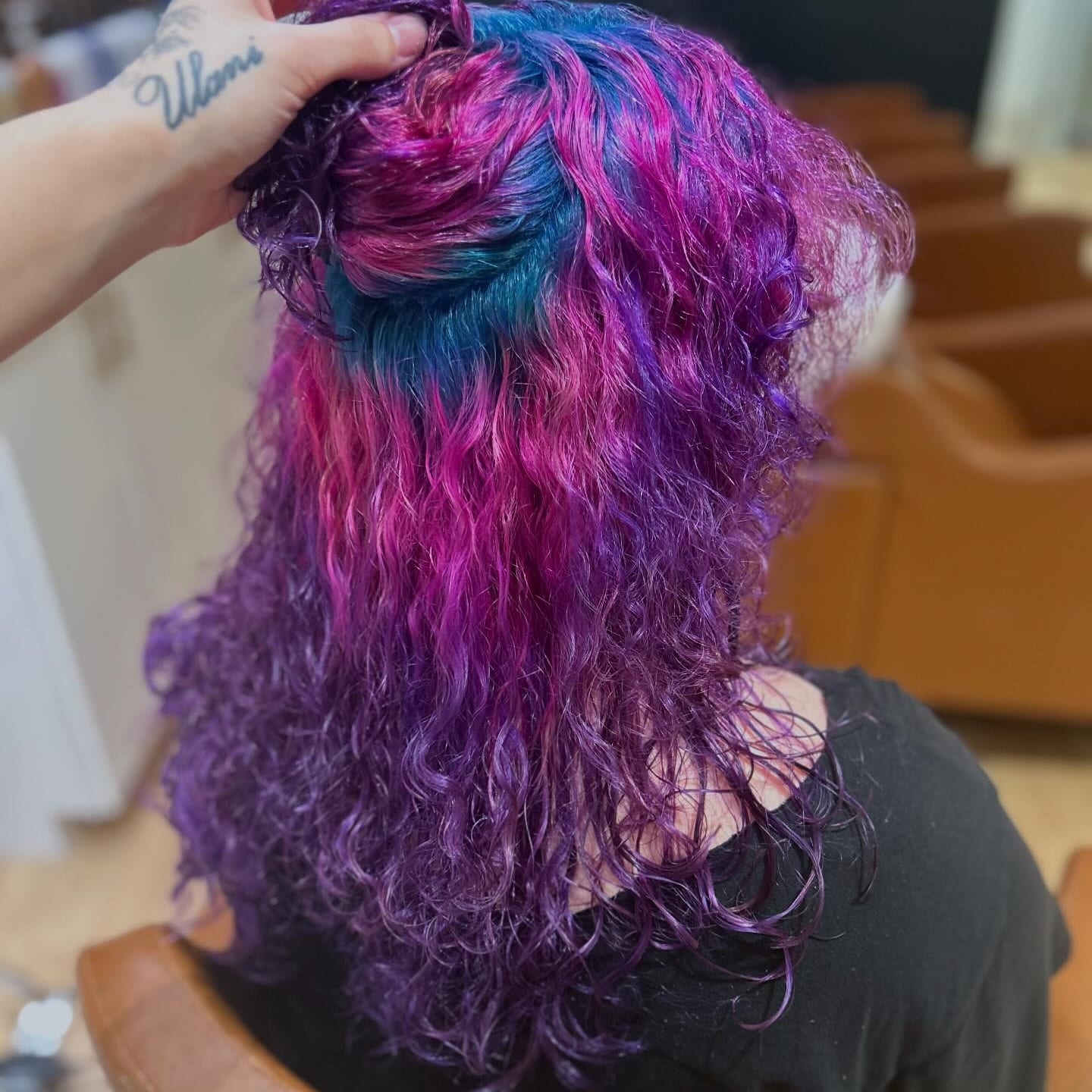 Curly hair in pink, blue and purple vivid color, the top section held up to show blue at the crown, at Canterbury & Co. in Fort Myers